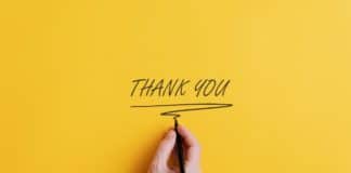 A person writing thank you on a yellow paper