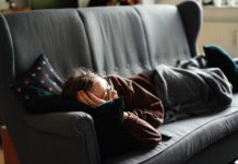 woman in pink jacket lying on gray couch